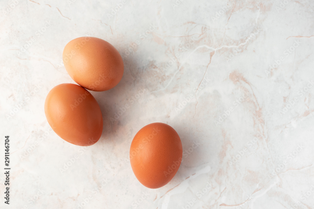 Three brown organic eggs on marble background, top view. Chicken free-range eggs, farm product Three brown organic eggs on marble background, top view. Chicken free-range eggs, farm product