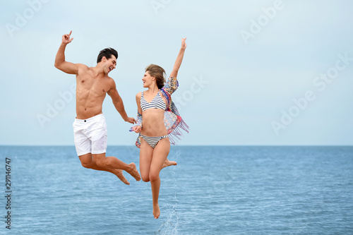 Happy young couple jumping together on sea beach. Space for text