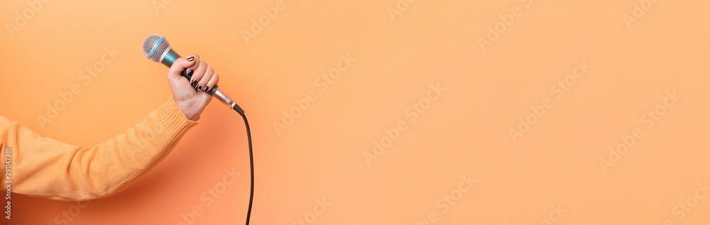 hand holding microphone over orange background, panoramic mock up image - obrazy, fototapety, plakaty 