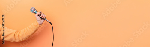 hand holding microphone over orange background, panoramic mock up image