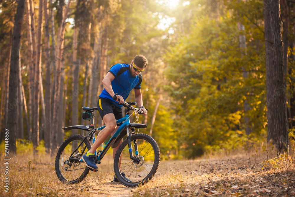 Happy bearded man cyclist rides in the sunny forest on a mountain bike. Adventure travel.