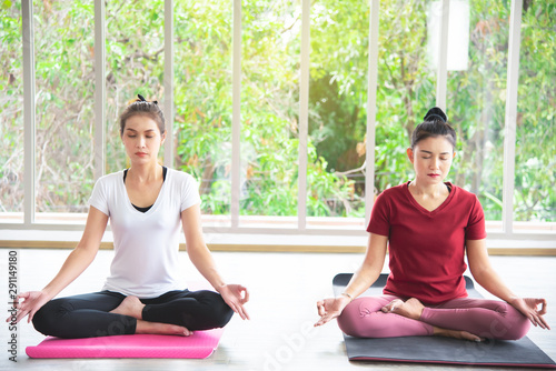 Two beautiful Asian women who are exercising, doing yoga in the room to practice their body exercises and breath control are popular concepts for body maintenance.