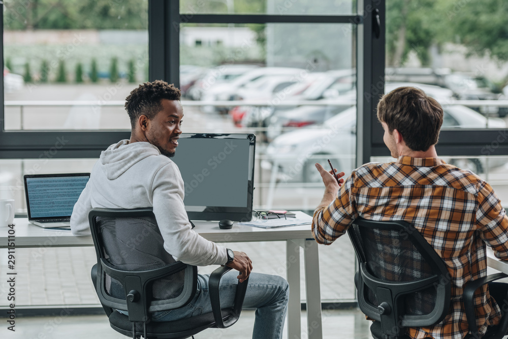 back view of young programmer talking to african american colleague in office back view of young programmer talking to african american colleague in office