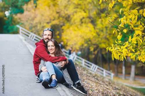 Beautiful happy young couple sit and embraces on roadside in autumn season.