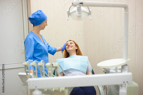 dentist in dental office talking with female patient and preparing for treatment.