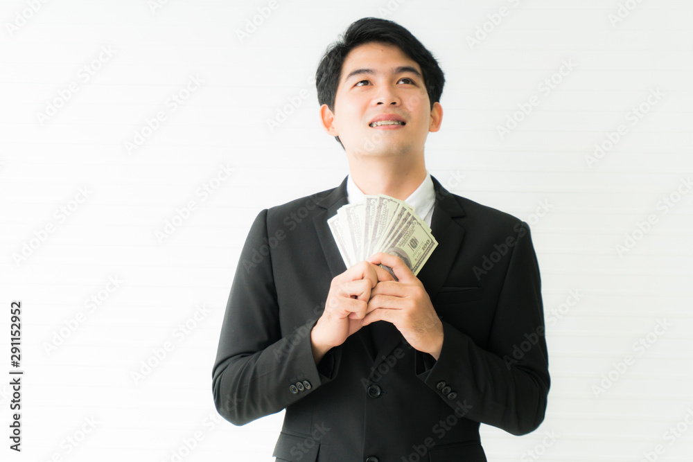 Portrait Asian young handsome businessman wearing black suit holding money dollars standing and smilling isolated on white background He is successful in the job with copy space Portrait Asian young handsome businessman wearing black suit holding money dollars standing and smilling isolated on white background He is successful in the job with copy space