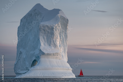Red sail and large iceberg landscape during mid night sun