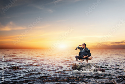 Alone businessman sitting on the stone in sea
