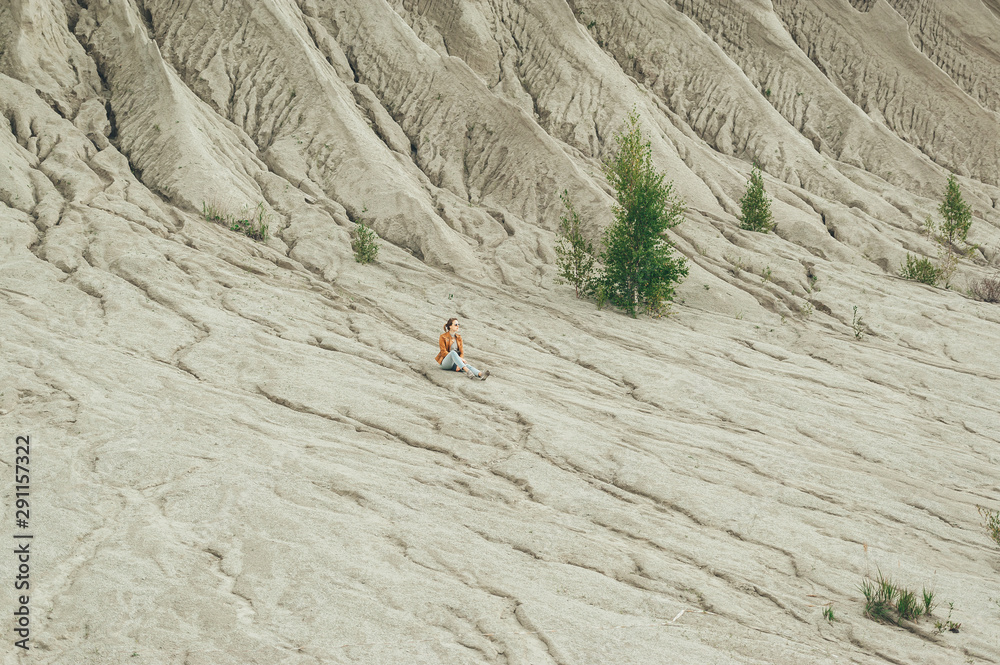 Young tourist girl sitting in the distance on a white sand geological and industrial district in Rummu. Estonia.