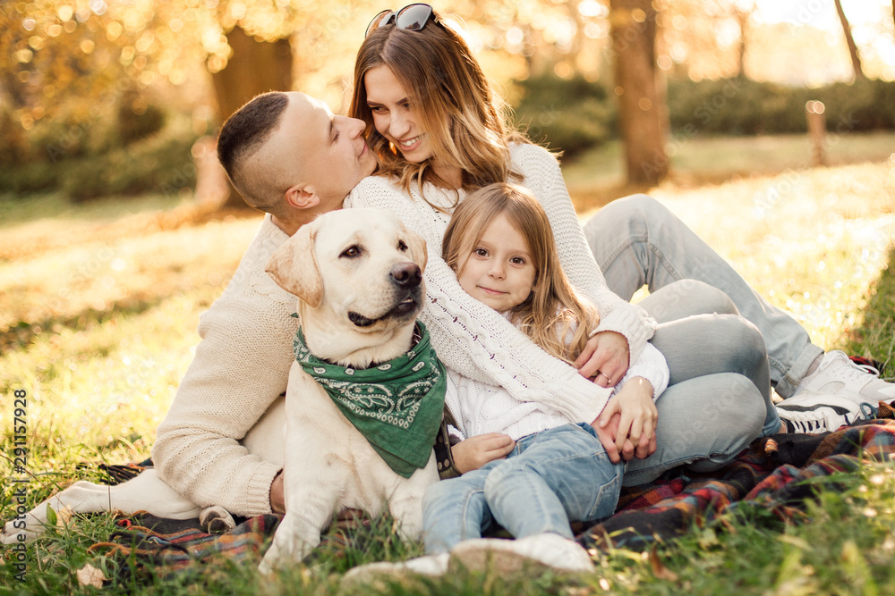Fototapeta premium Happy beautiful family with dog labrador is having fun are sitting on green grass in park.