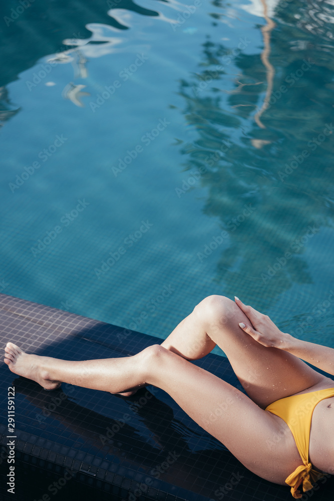 partial view of young woman sunbathing while lying near swimming pool partial view of young woman sunbathing while lying near swimming pool