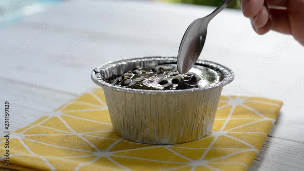 Eatting dark chocolate cake in foil cup with metal spoon on yellow table cloth. Delicious sweet bakery in coffee shop. Eatting dark chocolate cake in foil cup with metal spoon on yellow table cloth. Delicious sweet bakery in coffee shop.