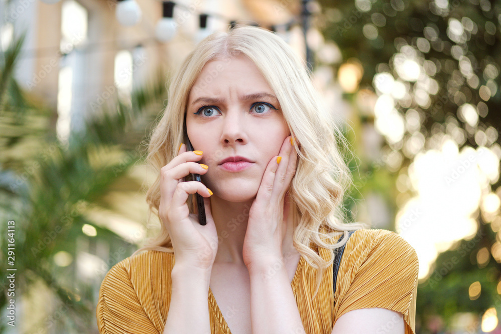 Portrait of serious blond girl amazedly looking away while talking on cellphone outdoor Portrait of serious blond girl amazedly looking away while talking on cellphone outdoor