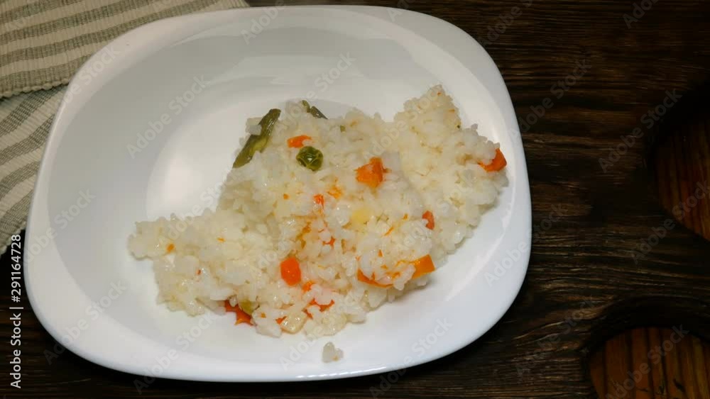 Homemade kitchen. Hot boiled rice and chopped tomatoes with sliced onions lie on white plate on wooden kitchen board. Appetizing Asian or European food. Vegetarian food. Close-up. Homemade kitchen. Hot boiled rice and chopped tomatoes with sliced onions lie on white plate on wooden kitchen board. Appetizing Asian or European food. Vegetarian food. Close-up.