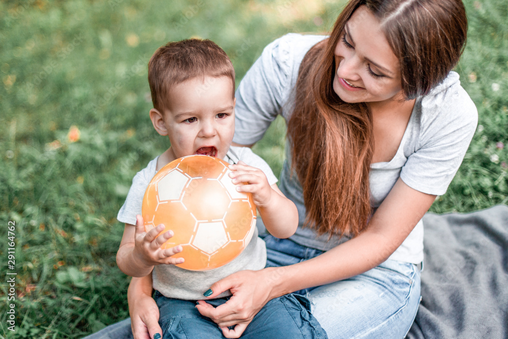 Mother with little son play with ball on green grass.