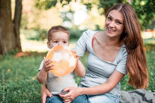 Mother with little son play with ball on green grass.