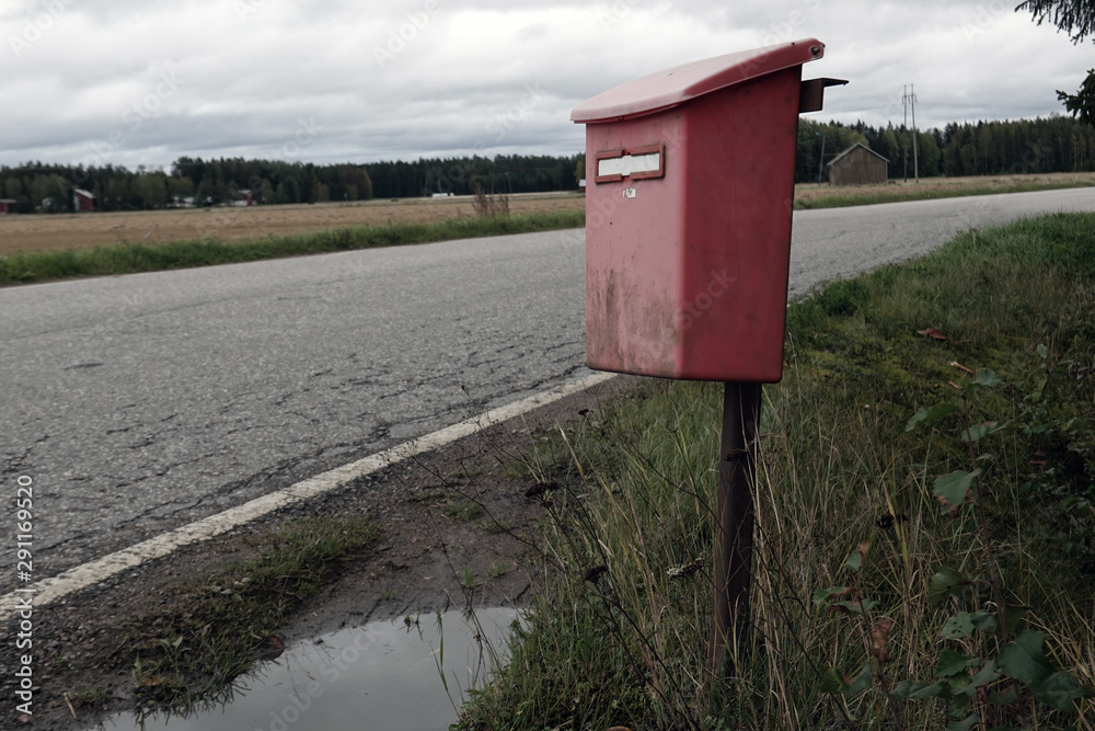 Old red weathered plastic mailbox in countryside.