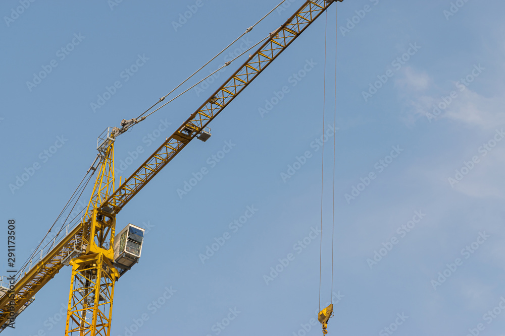 A yellow high-rise building crane against a blue sky builds multi-storey apartment buildings using modern technologies of metal, concrete and brick according to an architectural project