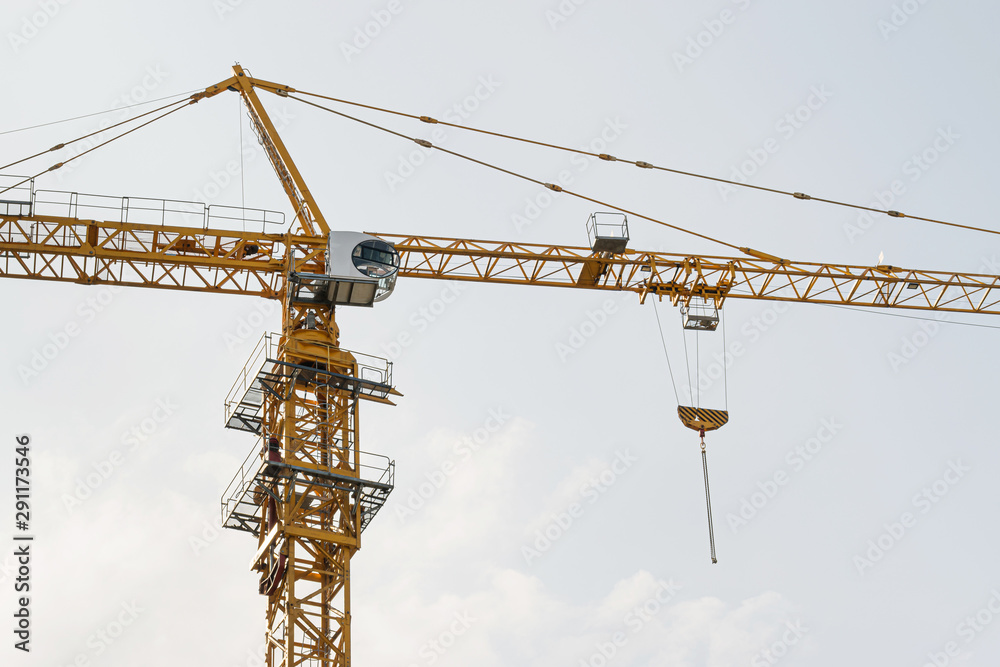 A yellow high-rise building crane against a blue sky builds multi-storey apartment buildings using modern technologies of metal, concrete and brick according to an architectural project A yellow high-rise building crane against a blue sky builds multi-storey apartment buildings using modern technologies of metal, concrete and brick according to an architectural project