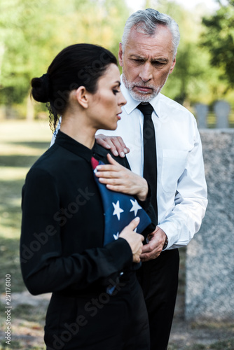 selective focus of bearded man looking at woman with american flag on funeral