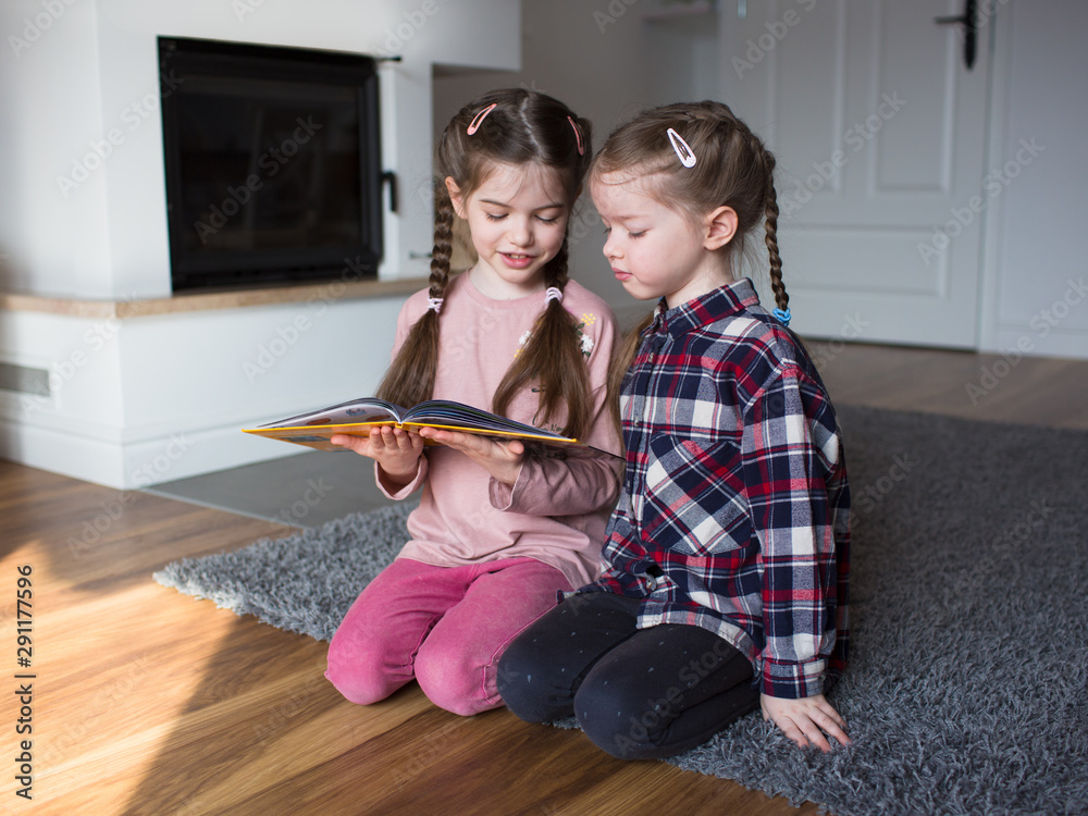 older sister is reading a book to younger sister older sister is reading a book to younger sister