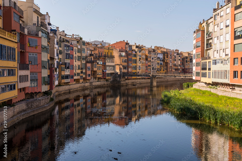 Colorful yellow and orange houses reflected in water river Onyar, in Girona, Catalonia, Spain.