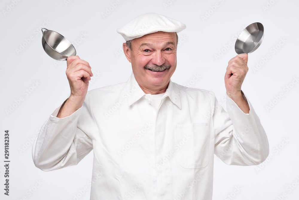 Mature hispanic man in white unifrom with fummy small kitchen pans. Studio shot Mature hispanic man in white unifrom with fummy small kitchen pans. Studio shot
