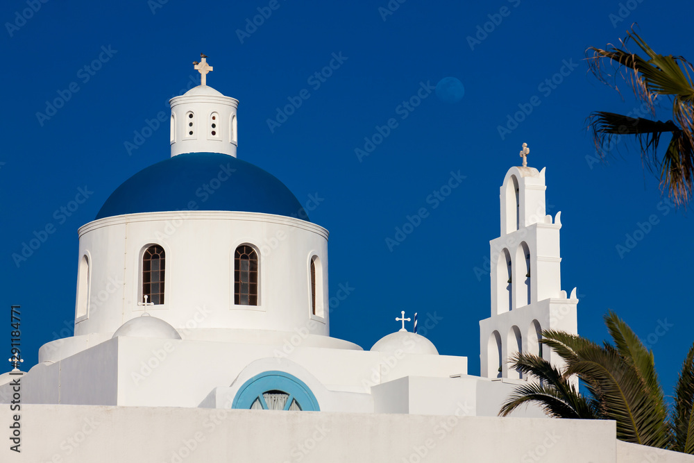 Dome and bell tower of the Church of Panagia Platsani and the moon located in Oia city at Santorini Island in a beautiful early spring day