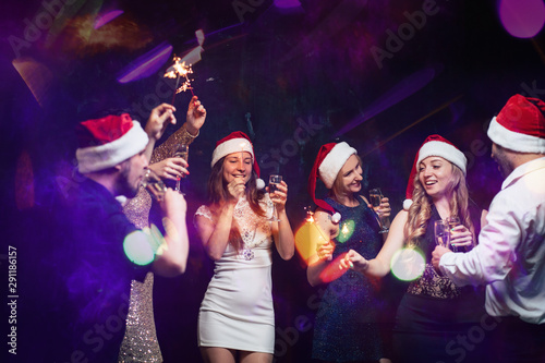 Christmas, dance party in night club, holiday, fun. Happy people celebrating New Year together. Company of friends in Santa caps dancing, celebration in motion