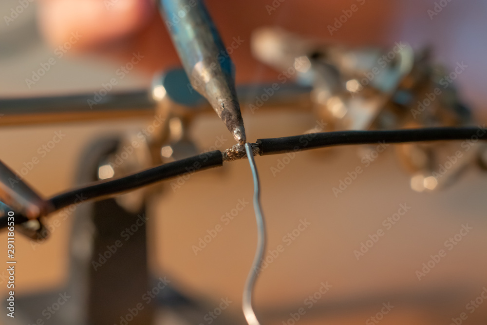 Two black wires being soldered together with a soldering iron Two black wires being soldered together with a soldering iron
