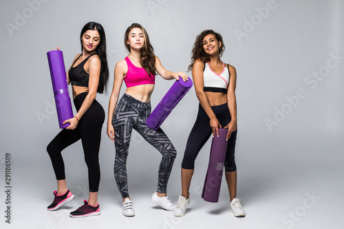 Three fitness young girls in sportswear standing isolated on white background. Girls smiling and looking to the camera.