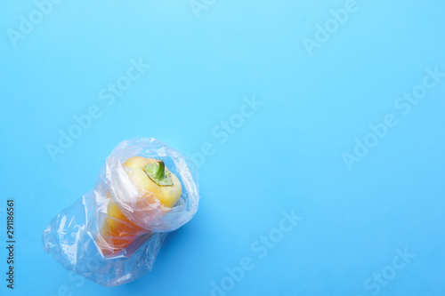 Recycling and environment concept: fresh food in plastic package. Yellow bell pepper wrapped in plastic bag in blue background.