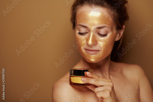 housewife with golden mask looking at bottle of face creme