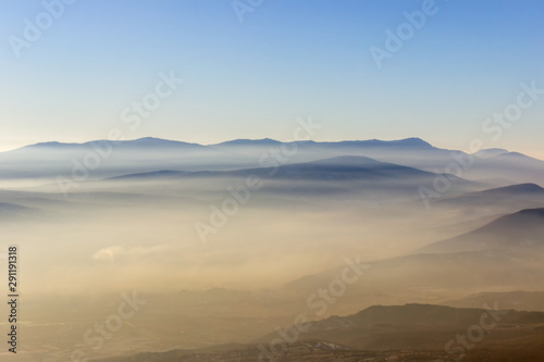 Soft, colorful, misty mountain layers and fields covered by golden fog during sunset © Nikola