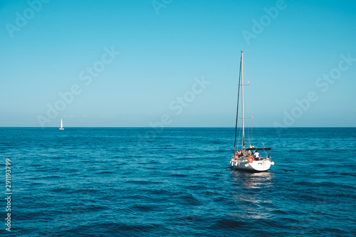 sailing boat with group of people on calm ocean on sunny day with clear blue sky