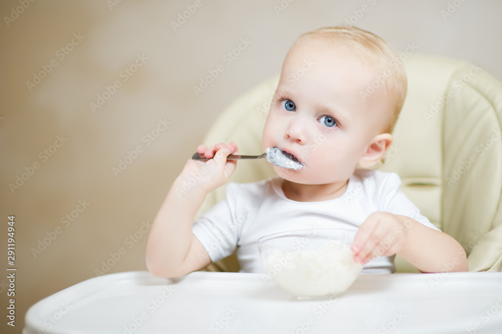 little child sits in a seat in the kitchen and eats rice porridge little child sits in a seat in the kitchen and eats rice porridge