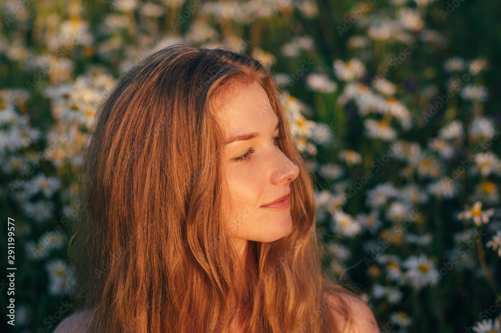 Fototapeta premium Portrait of pretty blond woman sitting in chamomile field