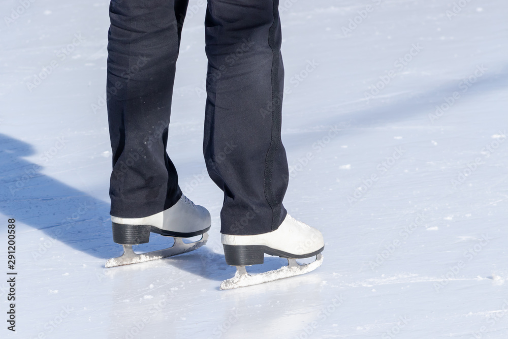 Ice skating, woman legs wearing white leather skates, training on a frosen snowy skating rink in winter close up Ice skating, woman legs wearing white leather skates, training on a frosen snowy skating rink in winter close up