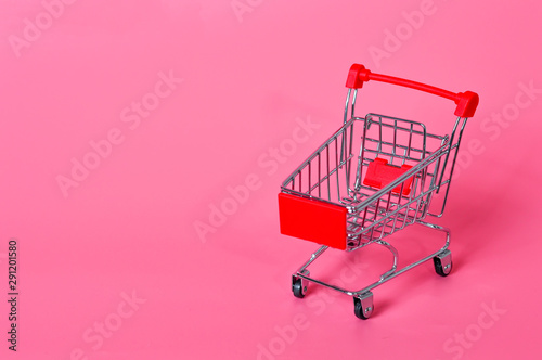 Small shopping cart on a pink background. Consumer basket. Shopping at a store.