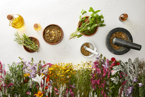 top view of mortars and pestles with herbal blends near flowers and bottles on white background photo