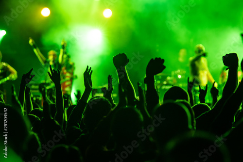 The crowd at concert. Summer music festival. Silhouettes of concert crowd in front of bright stage lights. Young people dancing and having fun at a summer festival party.