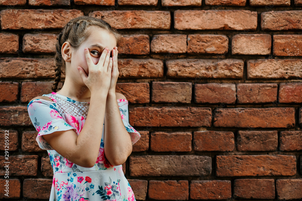A teenage girl smiles and covers her face with boats, with one eye looks through her fingers, a beautiful girl indulges and grimaces, a teenager against a brick wall A teenage girl smiles and covers her face with boats, with one eye looks through her fingers, a beautiful girl indulges and grimaces, a teenager against a brick wall