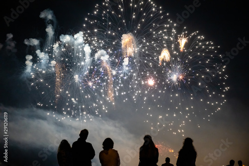 people look at the bright flashes of a festive firework in the night sky