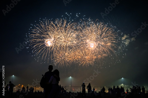 silhouettes of people watching fireworks in the background of bright flashes in the night sky