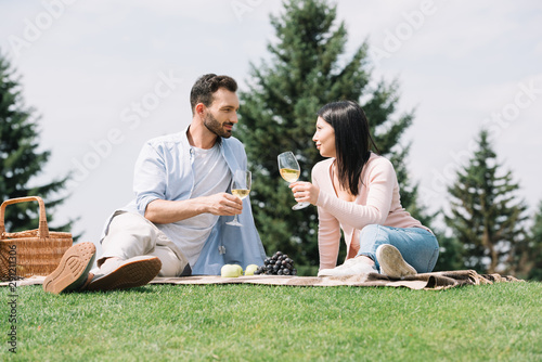 handsome man with disabled girlfriend holding glasses of white wine while sitting on blanket in park