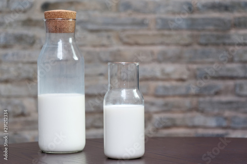Glass of milk and half bottle of milk on table with blur wall background.