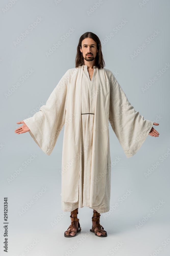 handsome bearded man in jesus robe standing with outstretched hands on grey