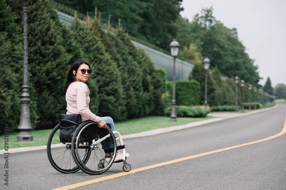 young disabled woman in sunglasses looking at camera while walking in park young disabled woman in sunglasses looking at camera while walking in park