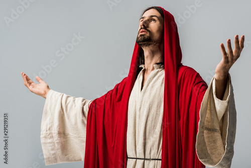 bearded man in red hood praying with outstretched hands isolated on grey