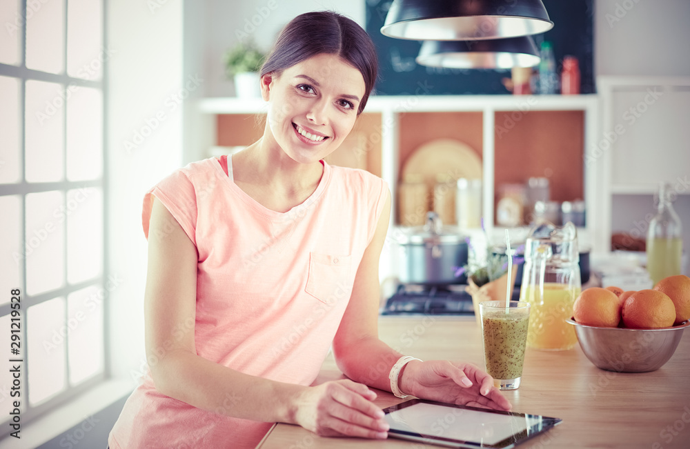 Beautiful young woman using a digital tablet in the kitchen Beautiful young woman using a digital tablet in the kitchen